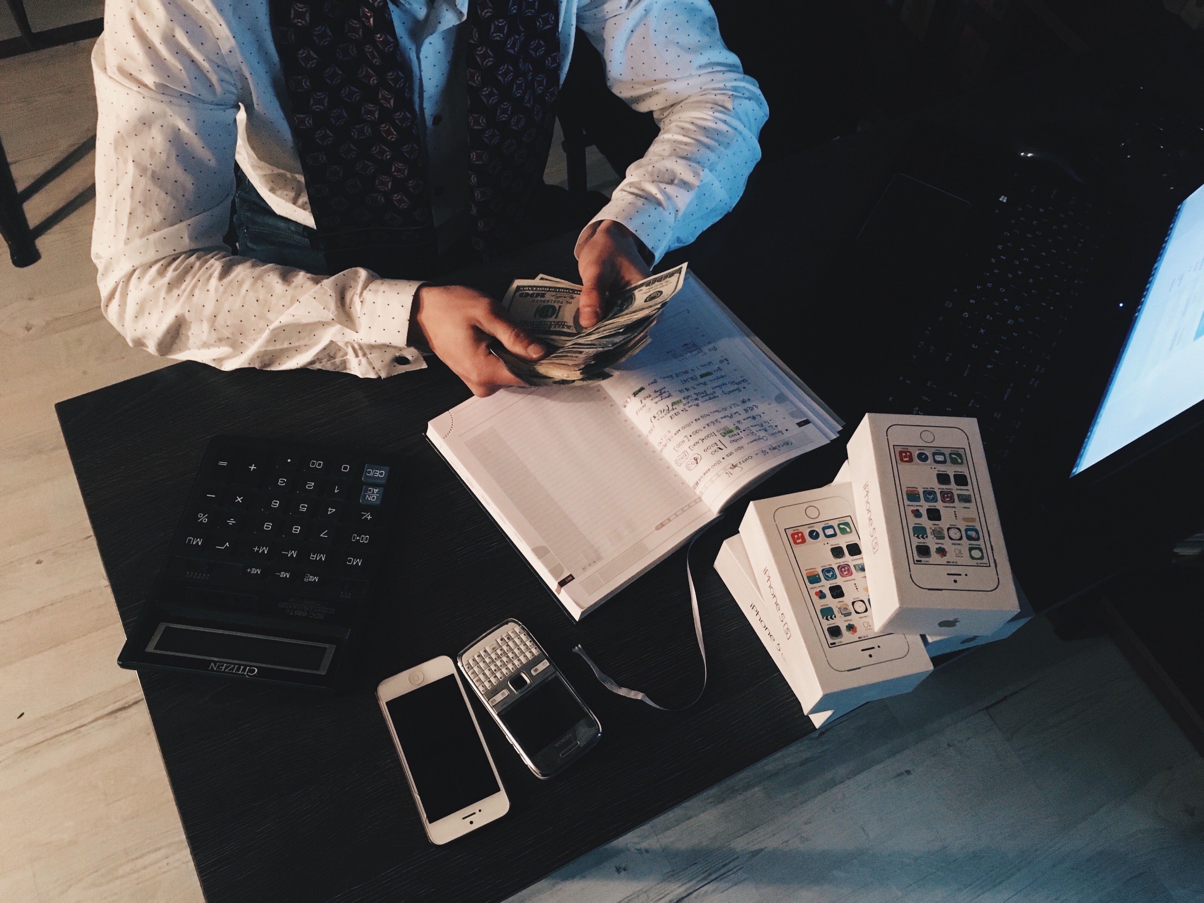 Person writing in a notebook next to a laptop while planning a budget