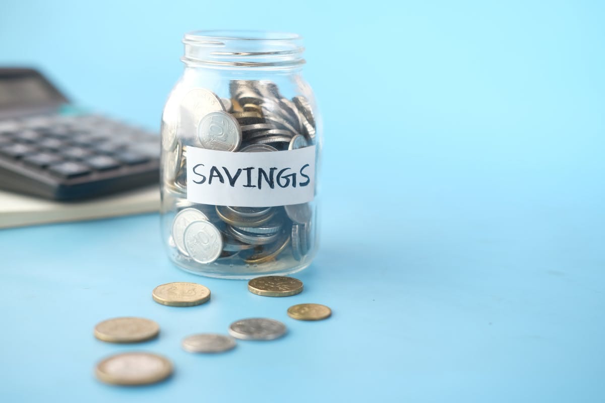Glass jar labeled Savings with coins beside a calculator